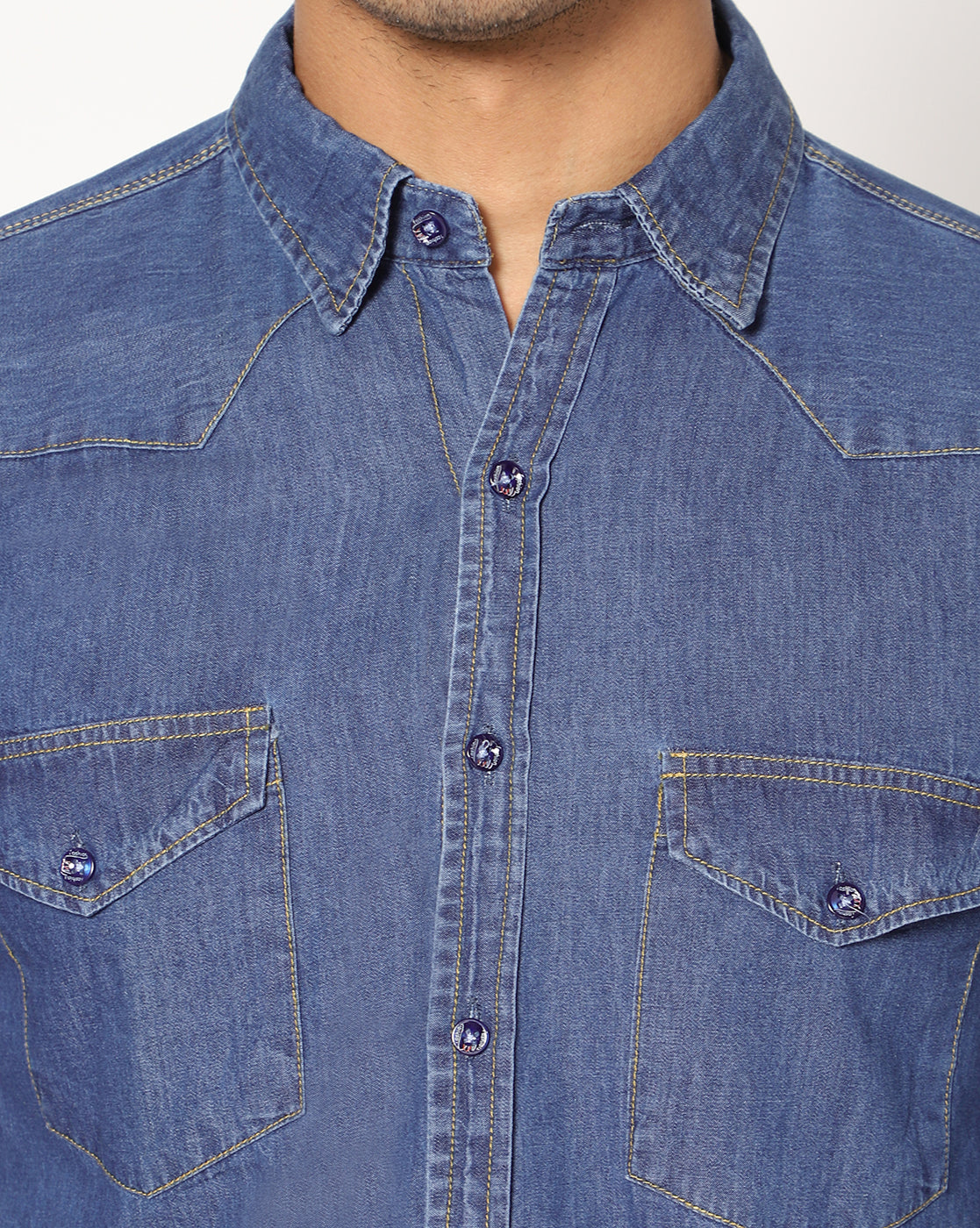 Close-up view of TCI Men’s Mid Blue Cotton Denim Shirt highlighting the detailed stitching, button-front closure, and textured cotton fabric. The close-up also shows the stylish chest pockets with button fastenings and the spread collar design.